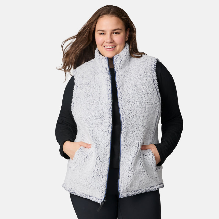 [Karissa is 5'9.5" wearing size 1X.] Women’s Free Country blue quilted vest with zip-front closure and zippered pockets—reverses to cozy sherpa for added warmth and texture. Worn over a black long-sleeve shirt and blue pants for a casual, transitional-weather look.