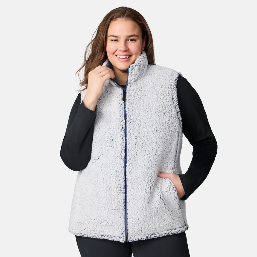 [Karissa is 5'9.5" wearing size 1X.] Women’s Free Country blue quilted vest with zip-front closure and zippered pockets—reverses to cozy sherpa for added warmth and texture. Worn over a black long-sleeve shirt and blue pants for a casual, transitional-weather look.