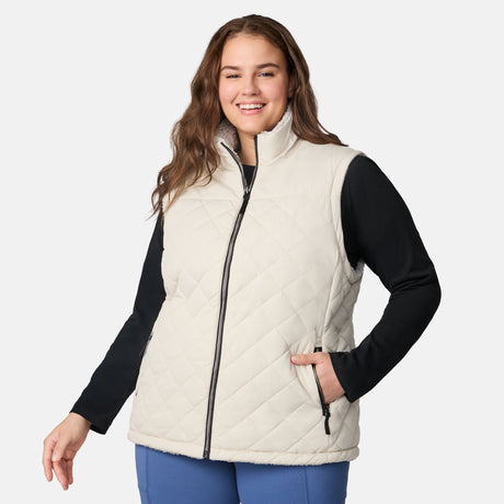 [Karissa is 5'9.5" wearing size 1X.] Women’s Free Country light beige quilted vest with zip-front closure and zippered pockets—reverses to cozy sherpa for added warmth and texture. Worn over a black long-sleeve shirt and blue pants for a casual, transitional-weather look.