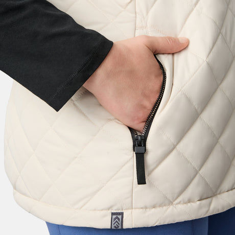 [Karissa is 5'9.5" wearing size 1X.] Women’s Free Country light beige quilted vest with zip-front closure and zippered pockets—reverses to cozy sherpa for added warmth and texture. Worn over a black long-sleeve shirt and blue pants for a casual, transitional-weather look.