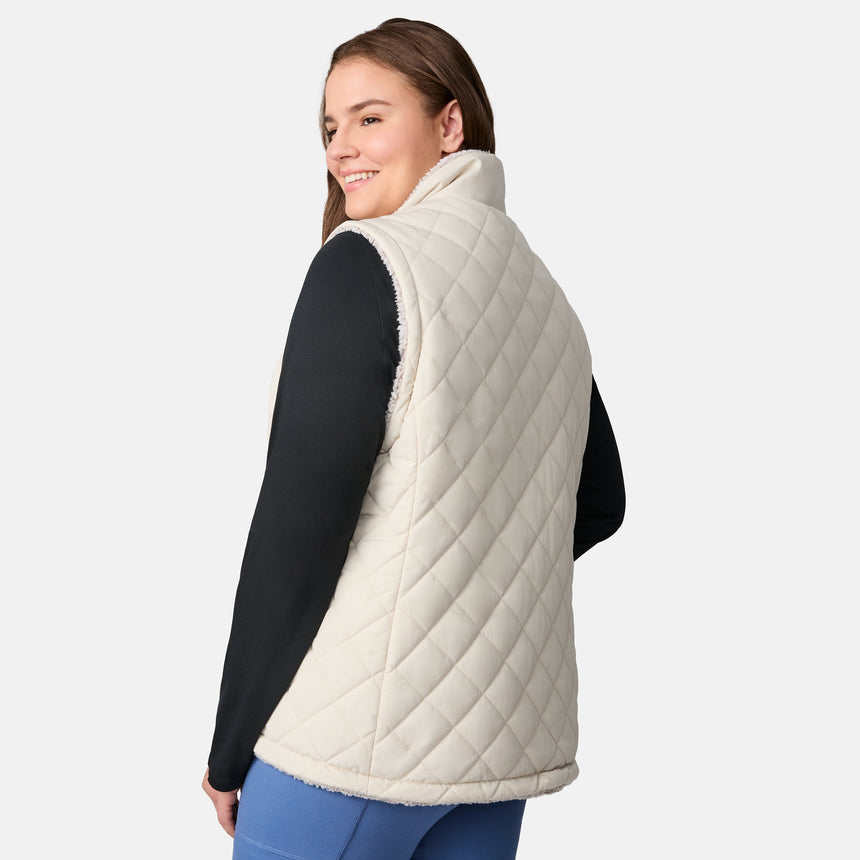 [Karissa is 5'9.5" wearing size 1X.] Women’s Free Country light beige quilted vest with zip-front closure and zippered pockets—reverses to cozy sherpa for added warmth and texture. Worn over a black long-sleeve shirt and blue pants for a casual, transitional-weather look.