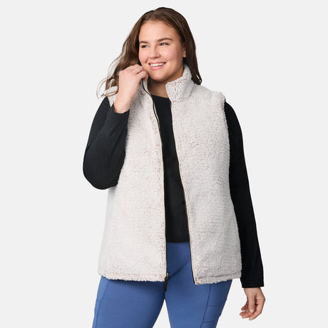 [Karissa is 5'9.5" wearing size 1X.] Women’s Free Country light beige quilted vest with zip-front closure and zippered pockets—reverses to cozy sherpa for added warmth and texture. Worn over a black long-sleeve shirt and blue pants for a casual, transitional-weather look.