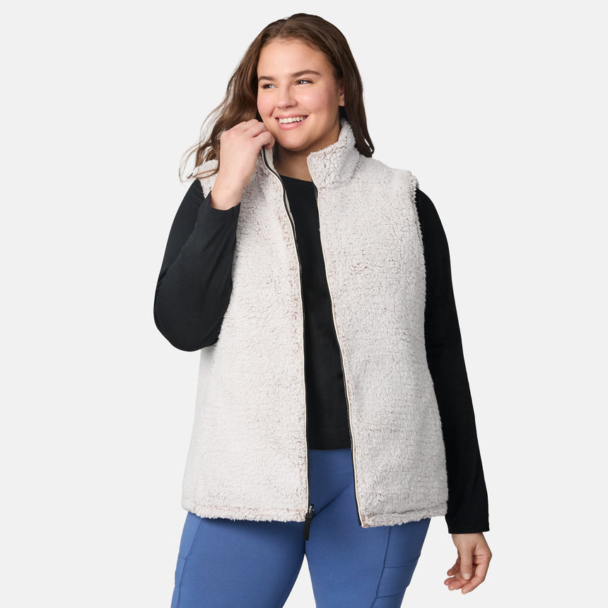 [Karissa is 5'9.5" wearing size 1X.] Women’s Free Country light beige quilted vest with zip-front closure and zippered pockets—reverses to cozy sherpa for added warmth and texture. Worn over a black long-sleeve shirt and blue pants for a casual, transitional-weather look.