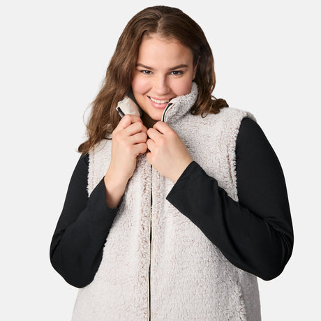 [Karissa is 5'9.5" wearing size 1X.] Women’s Free Country light beige quilted vest with zip-front closure and zippered pockets—reverses to cozy sherpa for added warmth and texture. Worn over a black long-sleeve shirt and blue pants for a casual, transitional-weather look.