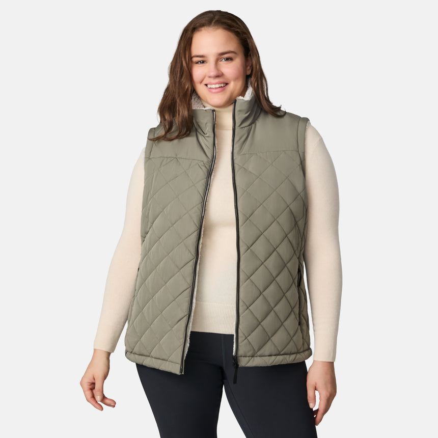 [Karissa is 5'9.5" wearing size 1X.]  Women’s Free Country light green diamond-quilted vest with zip-front closure and zippered pockets—reverses to cozy sherpa for added warmth and texture. Styled over a light long-sleeve shirt and dark pants for a versatile, cold-weather look.