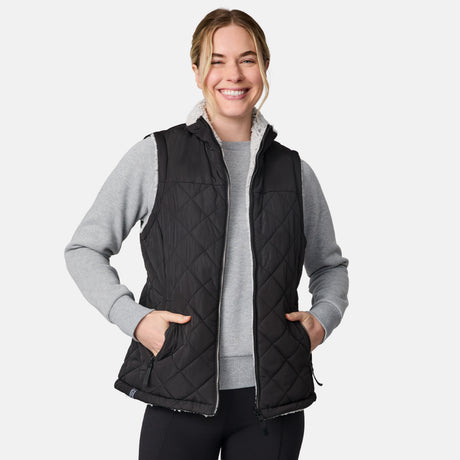 [CJ is 5'10" wearing size S.] Women’s Free Country black quilted vest with zip-front closure and dual zippered pockets—reversible to cozy sherpa for added warmth and versatile styling. Layered over a light gray long-sleeve shirt for a casual, cold-weather look.
