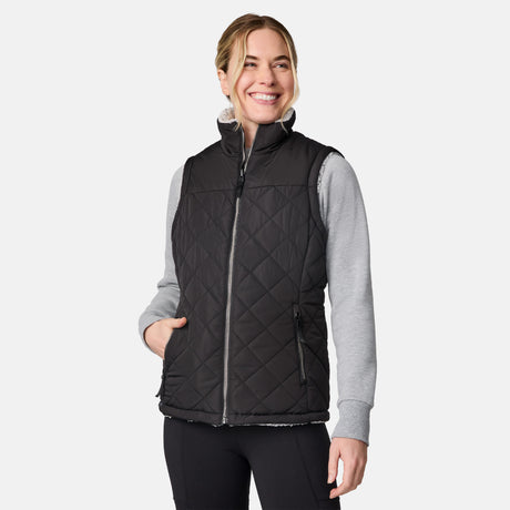 [CJ is 5'10" wearing size S.] Women’s Free Country black quilted vest with zip-front closure and dual zippered pockets—reversible to cozy sherpa for added warmth and versatile styling. Layered over a light gray long-sleeve shirt for a casual, cold-weather look.
