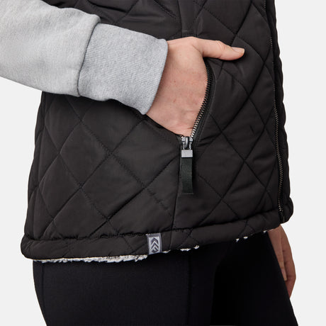 [CJ is 5'10" wearing size S.] Women’s Free Country black quilted vest with zip-front closure and dual zippered pockets—reversible to cozy sherpa for added warmth and versatile styling. Layered over a light gray long-sleeve shirt for a casual, cold-weather look.
