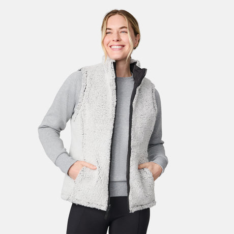[CJ is 5'10" wearing size S.] Women’s Free Country black quilted vest with zip-front closure and dual zippered pockets—reversible to cozy sherpa for added warmth and versatile styling. Layered over a light gray long-sleeve shirt for a casual, cold-weather look.