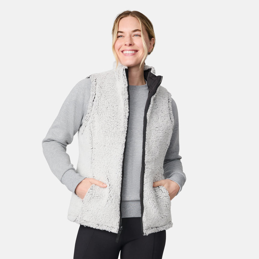 [CJ is 5'10" wearing size S.] Women’s Free Country black quilted vest with zip-front closure and dual zippered pockets—reversible to cozy sherpa for added warmth and versatile styling. Layered over a light gray long-sleeve shirt for a casual, cold-weather look.