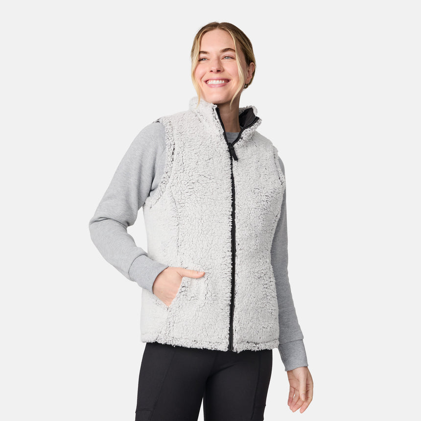 [CJ is 5'10" wearing size S.] Women’s Free Country black quilted vest with zip-front closure and dual zippered pockets—reversible to cozy sherpa for added warmth and versatile styling. Layered over a light gray long-sleeve shirt for a casual, cold-weather look.
