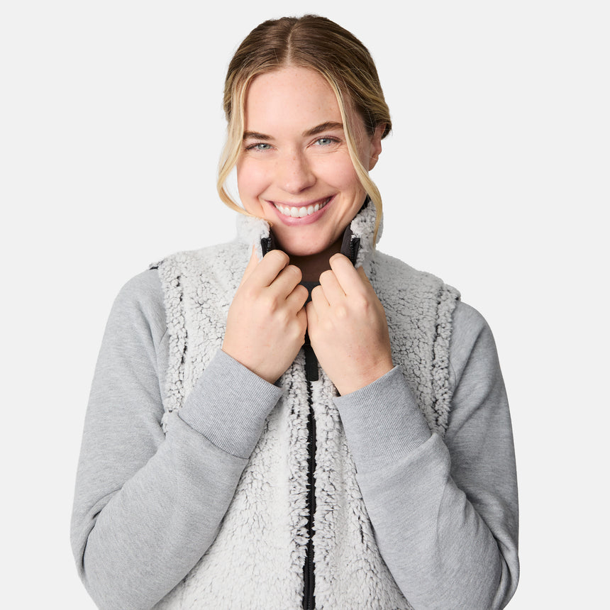 [CJ is 5'10" wearing size S.] Women’s Free Country black quilted vest with zip-front closure and dual zippered pockets—reversible to cozy sherpa for added warmth and versatile styling. Layered over a light gray long-sleeve shirt for a casual, cold-weather look.