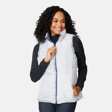 [Angelique is 5'10" wearing size S.] Women’s Free Country blue diamond-quilted vest with zip-front closure—reverses to cozy sherpa for added warmth and texture. Styled over a black long-sleeve shirt with one hand in pocket, set against a clean white background.