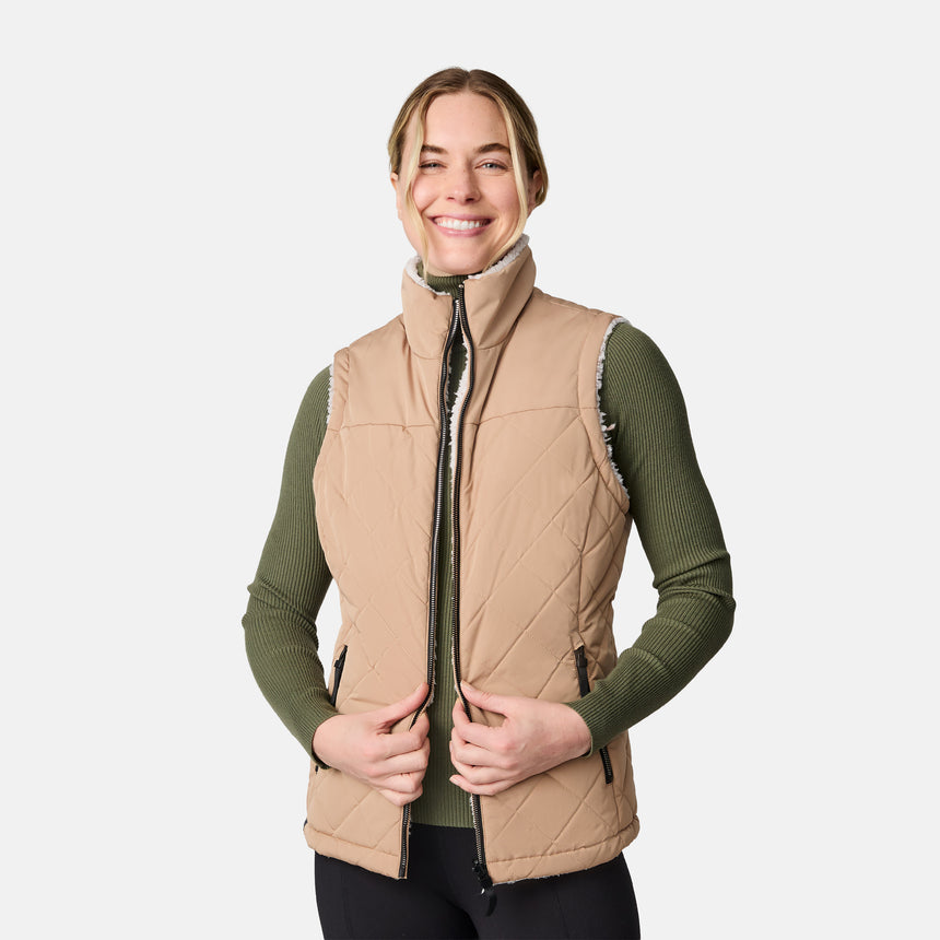 [CJ is 5'10" wearing size S.] Women’s Free Country beige diamond-quilted vest with zippered pockets and high collar—reverses to cozy sherpa for added warmth and texture. Layered over a green ribbed sweater and black pants for a stylish, cold-weather look.