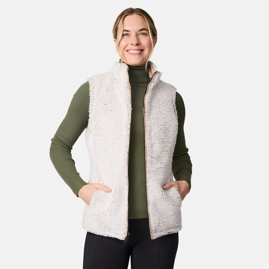 [CJ is 5'10" wearing size S.] Women’s Free Country beige diamond-quilted vest with zippered pockets and high collar—reverses to cozy sherpa for added warmth and texture. Layered over a green ribbed sweater and black pants for a stylish, cold-weather look.