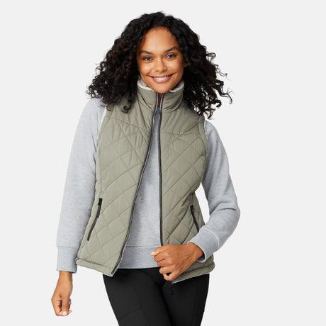 [Angelique is 5'10" wearing size S.] Women’s Free Country light green quilted vest with diamond pattern and black zippered pockets—reverses to cozy sherpa for added warmth and texture. Styled over a gray long-sleeve shirt and blue pants for a relaxed, transitional-weather look.