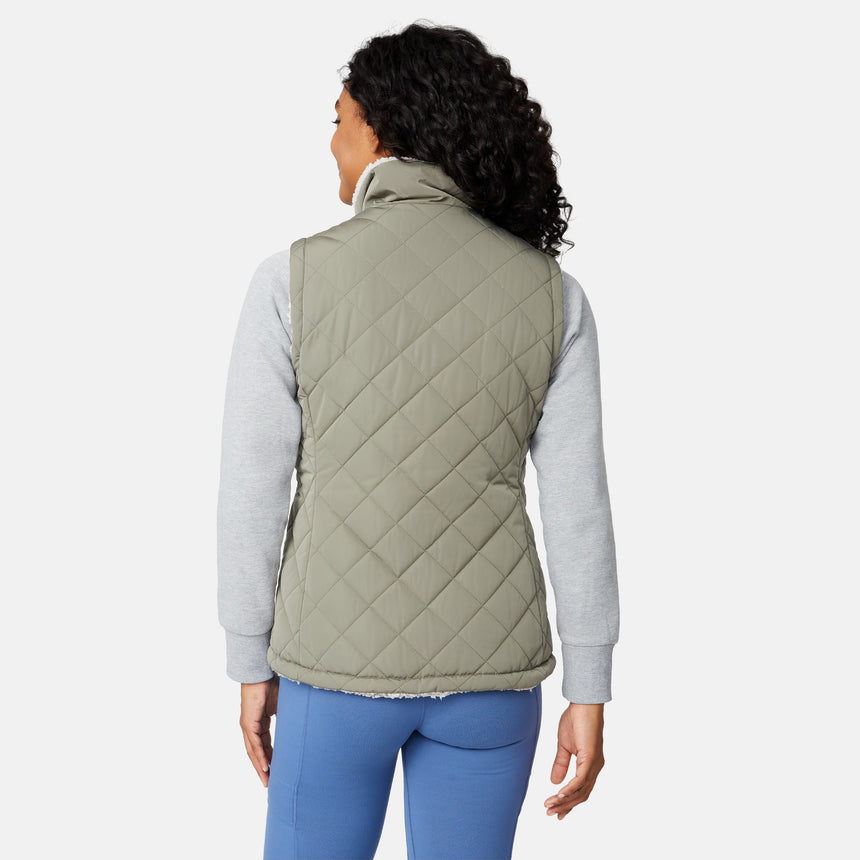 [Angelique is 5'10" wearing size S.] Women’s Free Country light green quilted vest with diamond pattern and black zippered pockets—reverses to cozy sherpa for added warmth and texture. Styled over a gray long-sleeve shirt and blue pants for a relaxed, transitional-weather look.