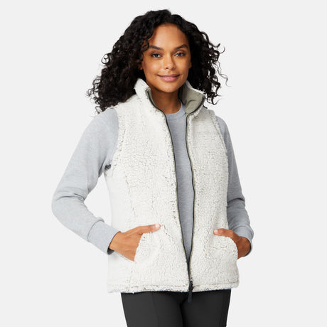 [Angelique is 5'10" wearing size S.] Women’s Free Country light green quilted vest with diamond pattern and black zippered pockets—reverses to cozy sherpa for added warmth and texture. Styled over a gray long-sleeve shirt and blue pants for a relaxed, transitional-weather look.