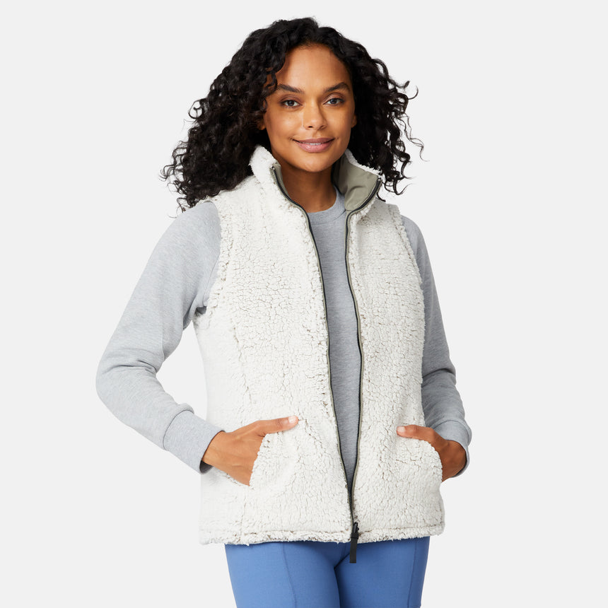 [Angelique is 5'10" wearing size S.] Women’s Free Country light green quilted vest with diamond pattern and black zippered pockets—reverses to cozy sherpa for added warmth and texture. Styled over a gray long-sleeve shirt and blue pants for a relaxed, transitional-weather look.