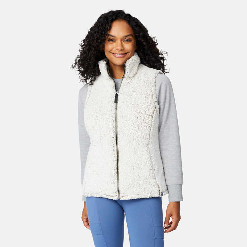 [Angelique is 5'10" wearing size S.] Women’s Free Country light green quilted vest with diamond pattern and black zippered pockets—reverses to cozy sherpa for added warmth and texture. Styled over a gray long-sleeve shirt and blue pants for a relaxed, transitional-weather look.