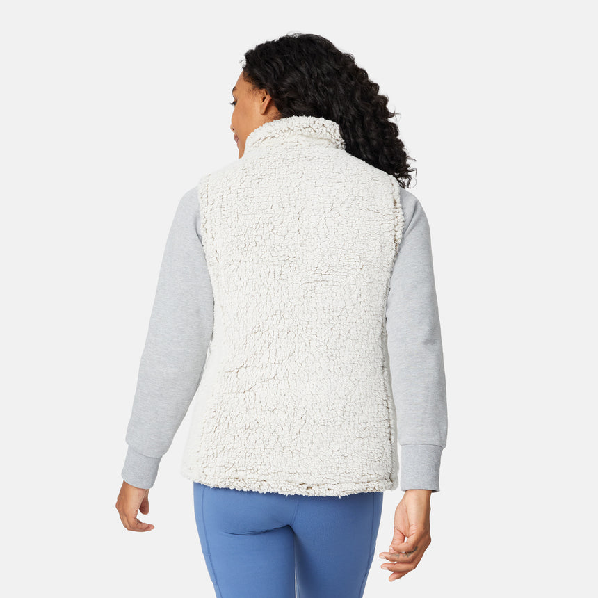 [Angelique is 5'10" wearing size S.] Women’s Free Country light green quilted vest with diamond pattern and black zippered pockets—reverses to cozy sherpa for added warmth and texture. Styled over a gray long-sleeve shirt and blue pants for a relaxed, transitional-weather look.