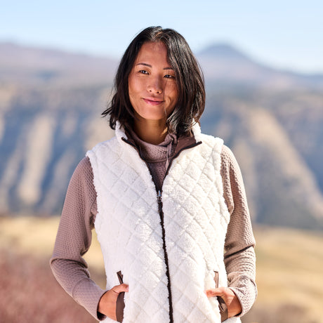 Woman wearing a white quilted vest with mountains in the background