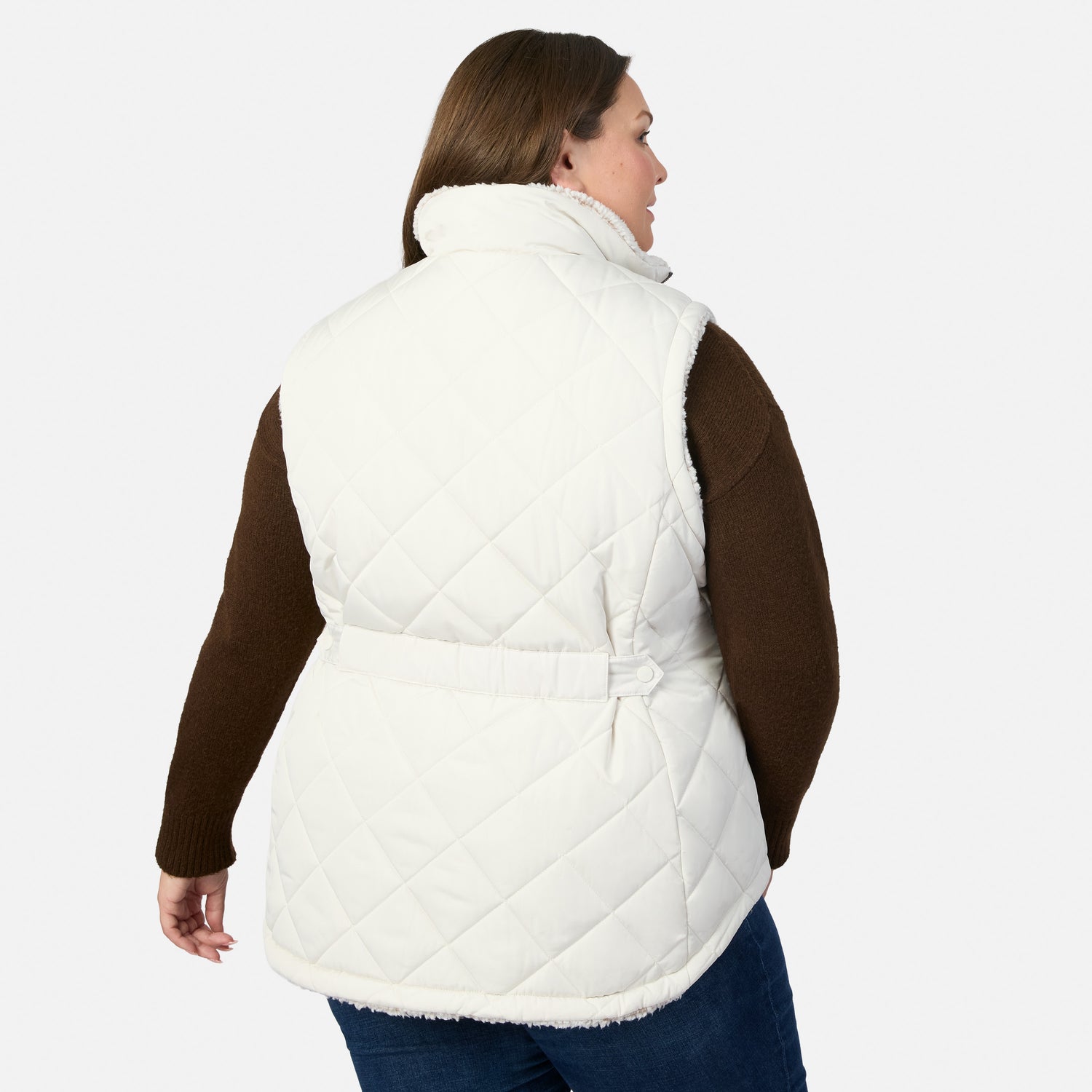 Back three-quarter view of woman in a white quilted Stratus Lite II reversible vest with sherpa lining over a brown sweater.