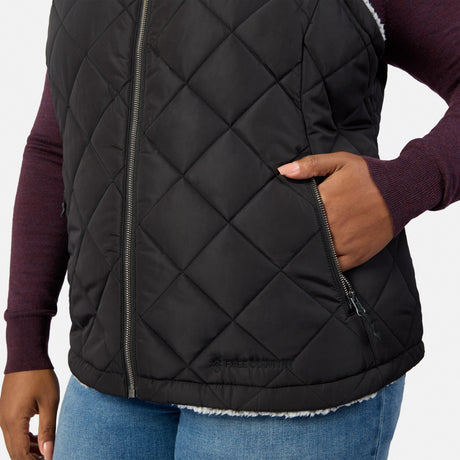 Close-up of black quilted vest showing front zipper and waist strap with snap button over burgundy sweater.