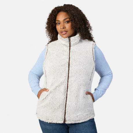 Front view of a plus-size woman wearing a cream sherpa reversible vest over a light blue long sleeve shirt.