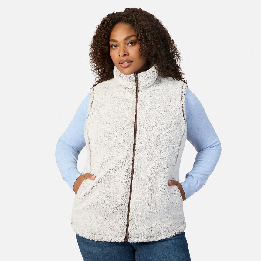Front view of a plus-size woman wearing a cream sherpa reversible vest over a light blue long sleeve shirt.