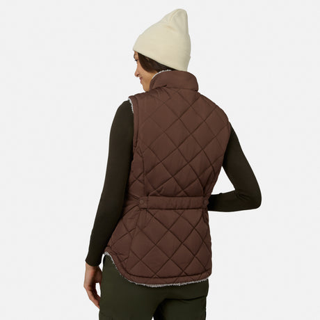 A person is seen from behind wearing a cream beanie, a dark long-sleeve top, and the Free Country Women’s Stratus Lite II Reversible Vest in quilted brown—crafted from recycled polyester—against a plain white background.