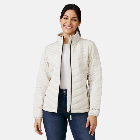 A smiling woman wears the Women's Stow & Go Packable Jacket by Clearance—a white quilted recycled polyester piece—over a white shirt and blue jeans, standing against a plain light background with her arms relaxed.