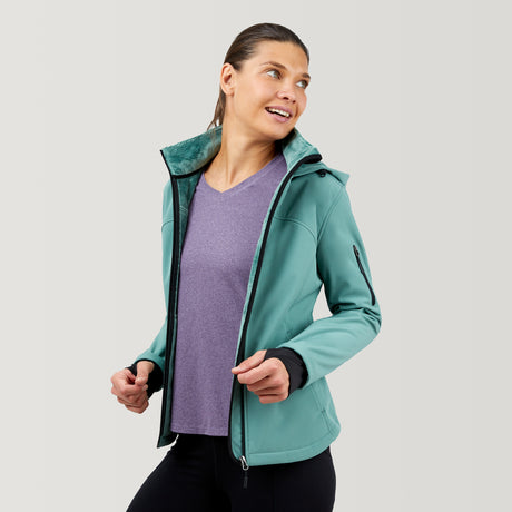 A woman with brown hair in a ponytail smiles and looks to the side, wearing the Clearance Women's FreeCycle® Super Softshell® Jacket over a lavender shirt and black pants against a plain light background.