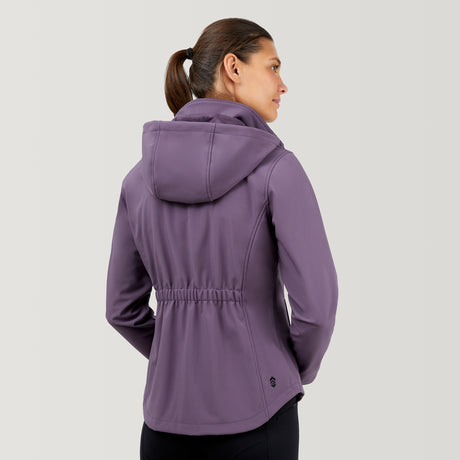 A woman with brown hair in a ponytail is seen from behind wearing the Clearance Women's FreeCycle® Super Softshell® Jacket in light purple, featuring water resistance and an elastic cinched waist, against a plain light gray background.