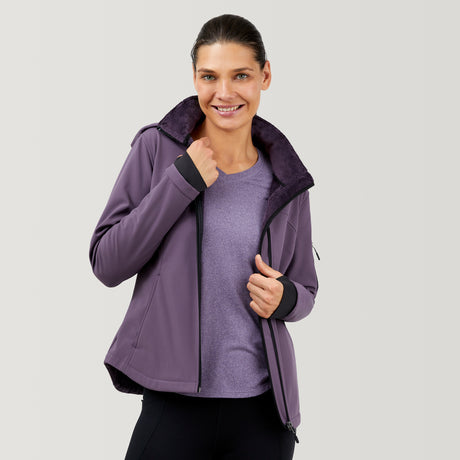A woman smiles while wearing the Clearance Women's FreeCycle® Super Softshell® Jacket with a furry collar over a purple shirt and black pants, standing against a light gray background.