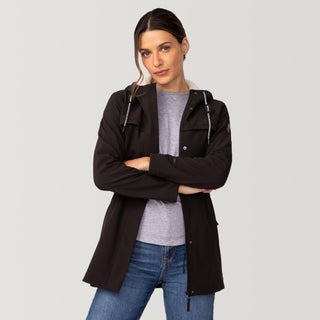 [Olga is 5’9" wearing size S.] Woman wearing Free Country Women's FreeCycle® Long Super Softshell® Jacket in black with a full front zipper opening, soft lining, cinched back waist, an attached hood with an adjustable drawcord, and water resistant and wind resistant performance fabric, light grey background. Best women’s jacket for chilly weather.