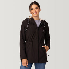 A woman stands smiling with one hand in her pocket against a plain light gray background, wearing the Clearance Women's FreeCycle® Long Super Softshell® Jacket in black and blue jeans.