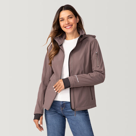 [Olga is 5’9” wearing a size Small.] Woman wearing Free Country Women's Aeris II Super Softshell® Jacket in light brown with a full front zipper opening, soft lining, detachable hood, and water resistant and wind resistant stretch performance fabric, light grey background. Perfect women’s  jacket for fall weather.