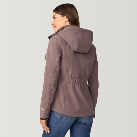 [Olga is 5’9” wearing a size Small.] Woman wearing Free Country Women's Aeris II Super Softshell® Jacket in light brown with a full front zipper opening, soft lining, detachable hood, and water resistant and wind resistant stretch performance fabric, light grey background. Perfect women’s  jacket for fall weather.