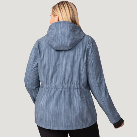 A woman with long blonde hair is seen from the back, wearing the Free Country Women's Plus Size Aeris II Super Softshell® Jacket in blue-gray and black pants, set against a plain light gray background.