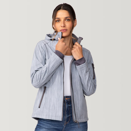 A woman wearing a light blue Free Country Women’s Aeris II Super Softshell® Jacket, featuring a chevron pattern, a zip-up hood, and dark gray accents.