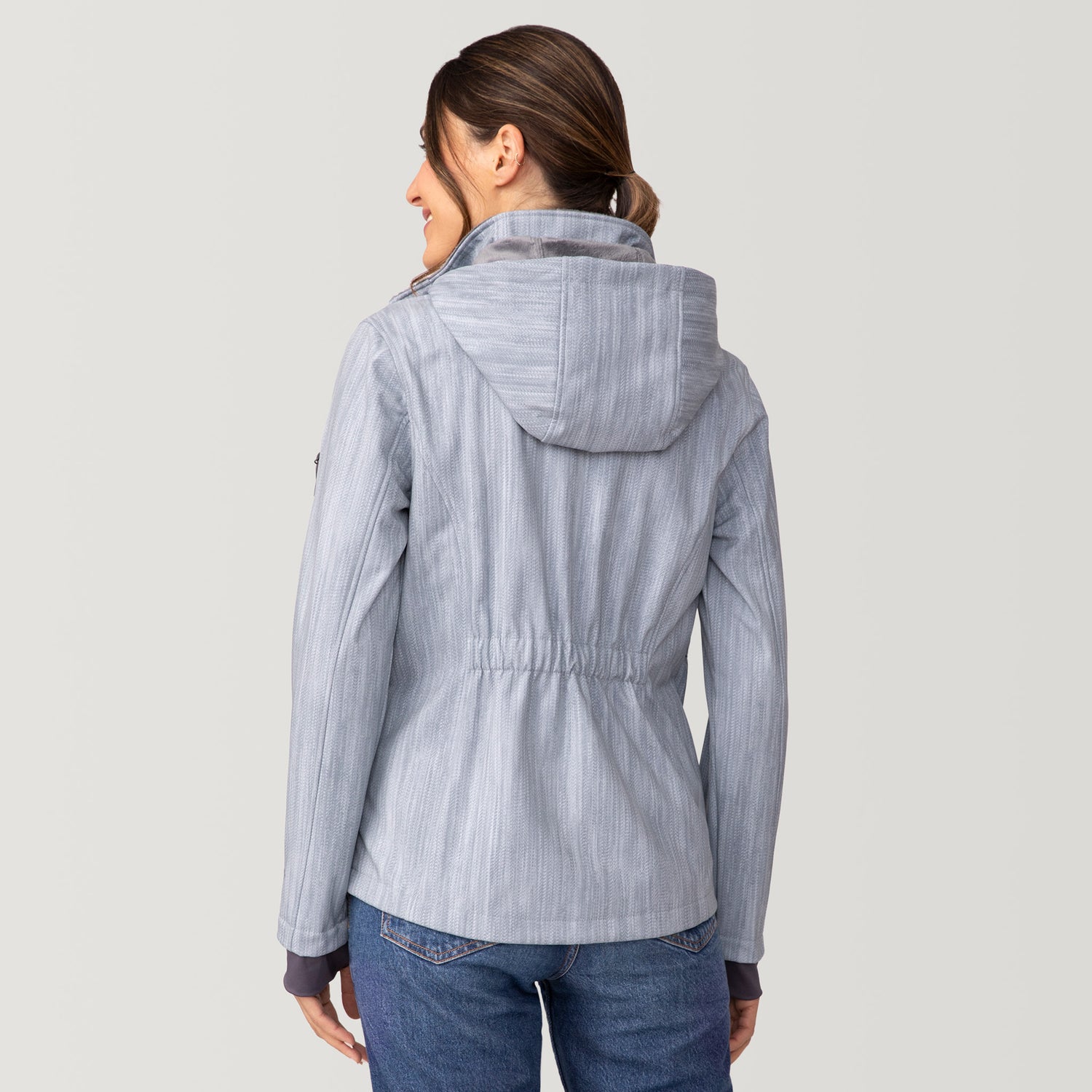 Back view of a woman wearing a light blue, water-resistant Women’s Aeris II Super Softshell® Jacket featuring a subtle herringbone pattern and a cinched waist.