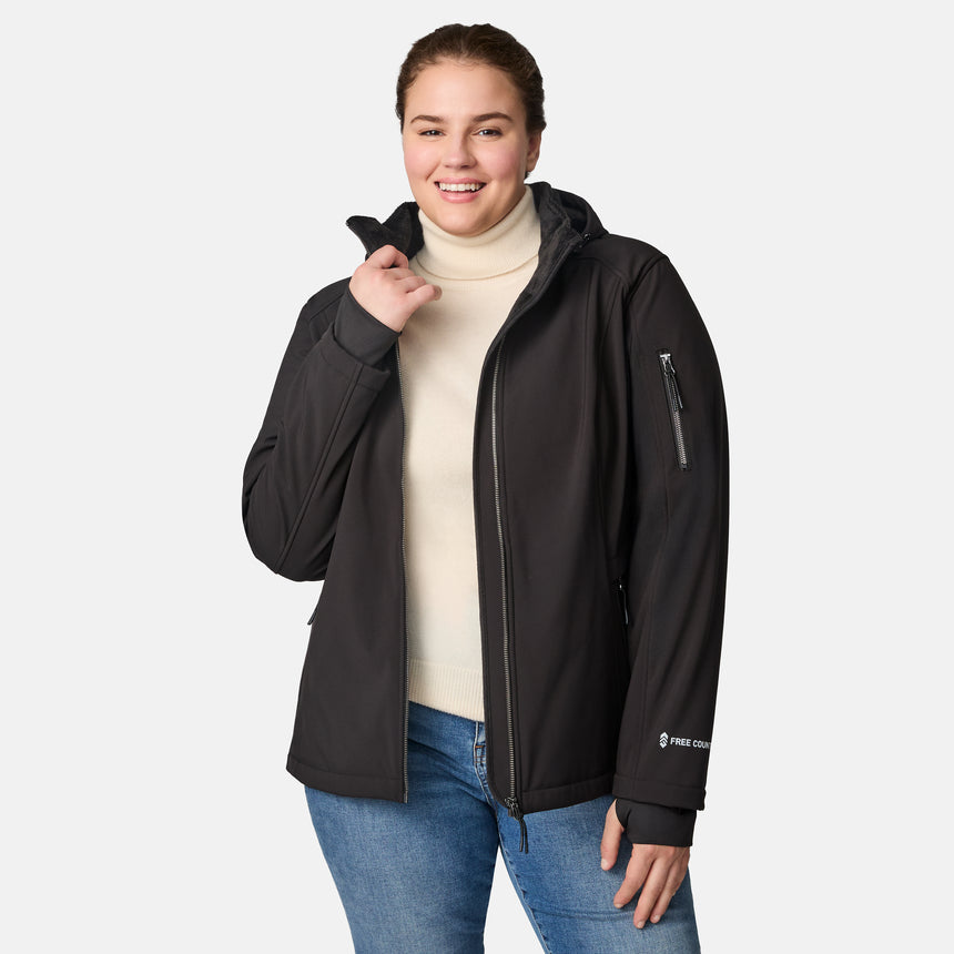 [Karissa is 5'9.5" wearing size 1X.] Woman wearing Free Country black hooded softshell jacket with sleeve zip pocket; worn over blue jeans, shown with raised arms to display fit and structure.