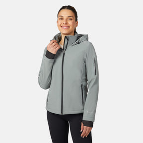 A woman stands smiling against a plain white background, wearing the Free Country Women's StormTech Super Softshell® Jacket in light gray with black trim and matching black leggings.