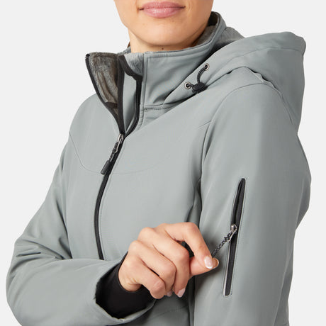 A woman wearing a Free Country Women's StormTech Super Softshell® Jacket in light gray is shown unzipping a small pocket on the sleeve, highlighting the jacket's outdoor design and her hand, with her face partially visible.