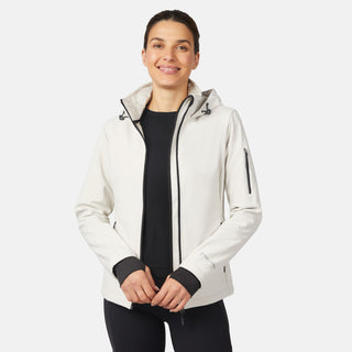 A woman smiles in a Free Country Women's StormTech Super Softshell® Jacket, white and water resistant, layered over a black top and pants, standing against a plain light background.