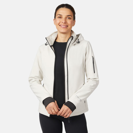 A woman smiles in a Free Country Women's StormTech Super Softshell® Jacket, white and water resistant, layered over a black top and pants, standing against a plain light background.
