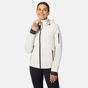 A woman smiles in the Free Country Women's StormTech Super Softshell® Jacket, featuring water-resistant white fabric with black zippers and cuffs, paired with black pants against a plain white background.