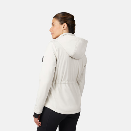 A woman with dark braided hair wears the Free Country Women's StormTech Super Softshell® Jacket and black leggings, standing against a white background, facing away and looking over her left shoulder.