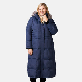[Lola is 5'10.5" wearing a size 1X.] Woman wearing Free Country Women's Plus Size Full Length Splendor Down Jacket in navy with a full front zipper opening, lower pockets, calf length, a detachable hood with faux fur trim, and water resistant and wind resistant stretch performance fabric, light grey background. Best women’s jacket for winter weather.